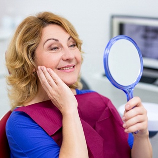 An older woman looking at her smile in the mirror at the dentist’s office