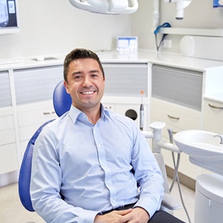Hombre sonriendo en el sillón dental vistiendo camisa con cuello