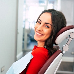Mujer en camisa roja sonriendo mientras está sentado en el sillón dental