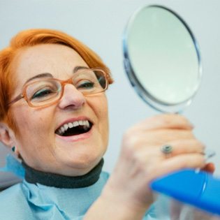 A senior woman admiring her dentures in a hand mirror  