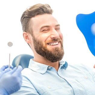 A young male with a beard smiling over his new appearance after receiving treatment for problem areas within his mouth