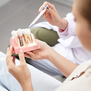 A dental professional showing a patient a cross-section model of a dental implant sitting next to healthy, natural teeth