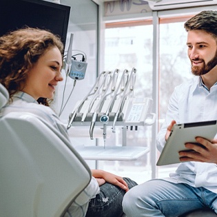 A dentist showing a patient an image on a tablet while discussing the benefits of full-mouth reconstruction