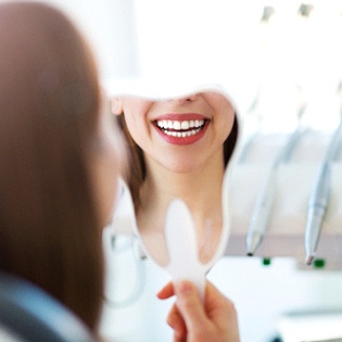 A woman seated in the dentist’s chair looking at her brighter smile after undergoing teeth whitening treatment