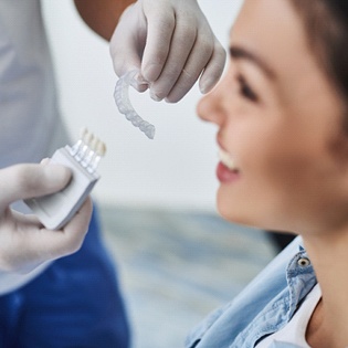 A woman smiling while her dentist holds an Invisalign aligner