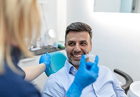 Man in dental chair smiling at dentist approaching with Invisalign
