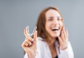 Laughing woman blurry in background holding Invisalign to foreground