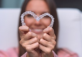 Woman blurry in background holding Invisalign in heart-shape in foreground