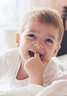 a toddler smiling with finger in mouth near Dumont