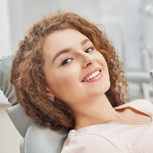 Mujer en camisa roja sonriendo mientras está sentado en el sillón dental