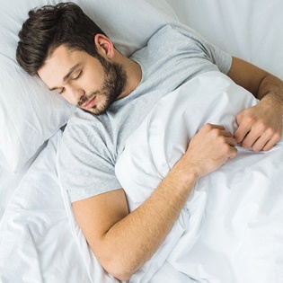 A man lying asleep in his bed after undergoing wisdom teeth removal