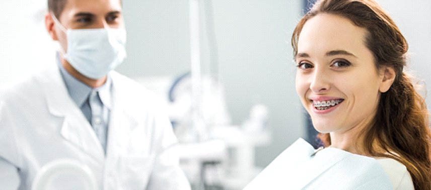 A female patient smiling with her traditional braces in Bergenfield showing while a dentist wearing a mask looks on