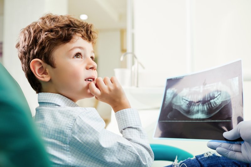 a little boy looks at his dentist while viewing his dental x-rays 