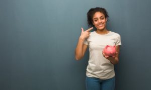 Patient pointing towards her smile and also holding a piggy bank