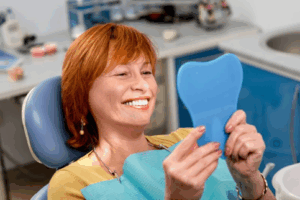 Woman in patient’s chair smiles at a small mirror